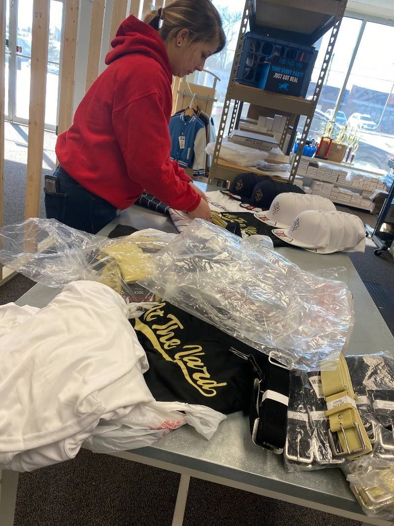 A young girl in a red hoodie is sitting at a table packing shirts.