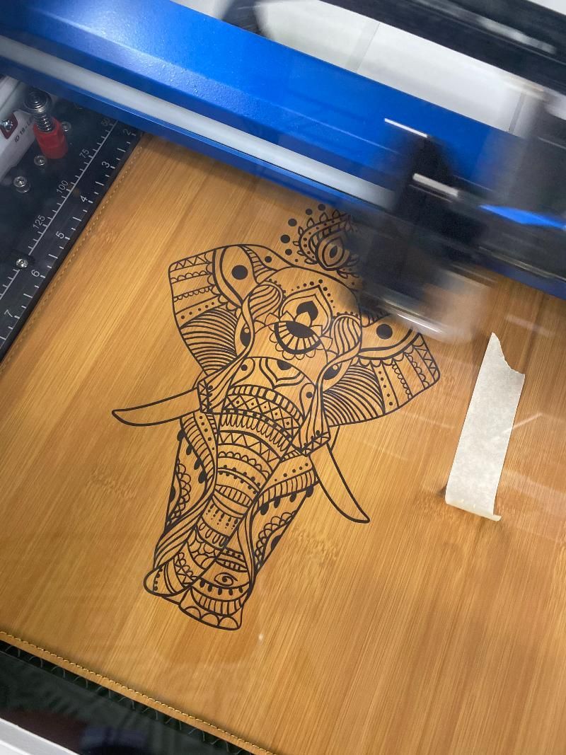 A machine is cutting a picture of an elephant on a wooden surface.