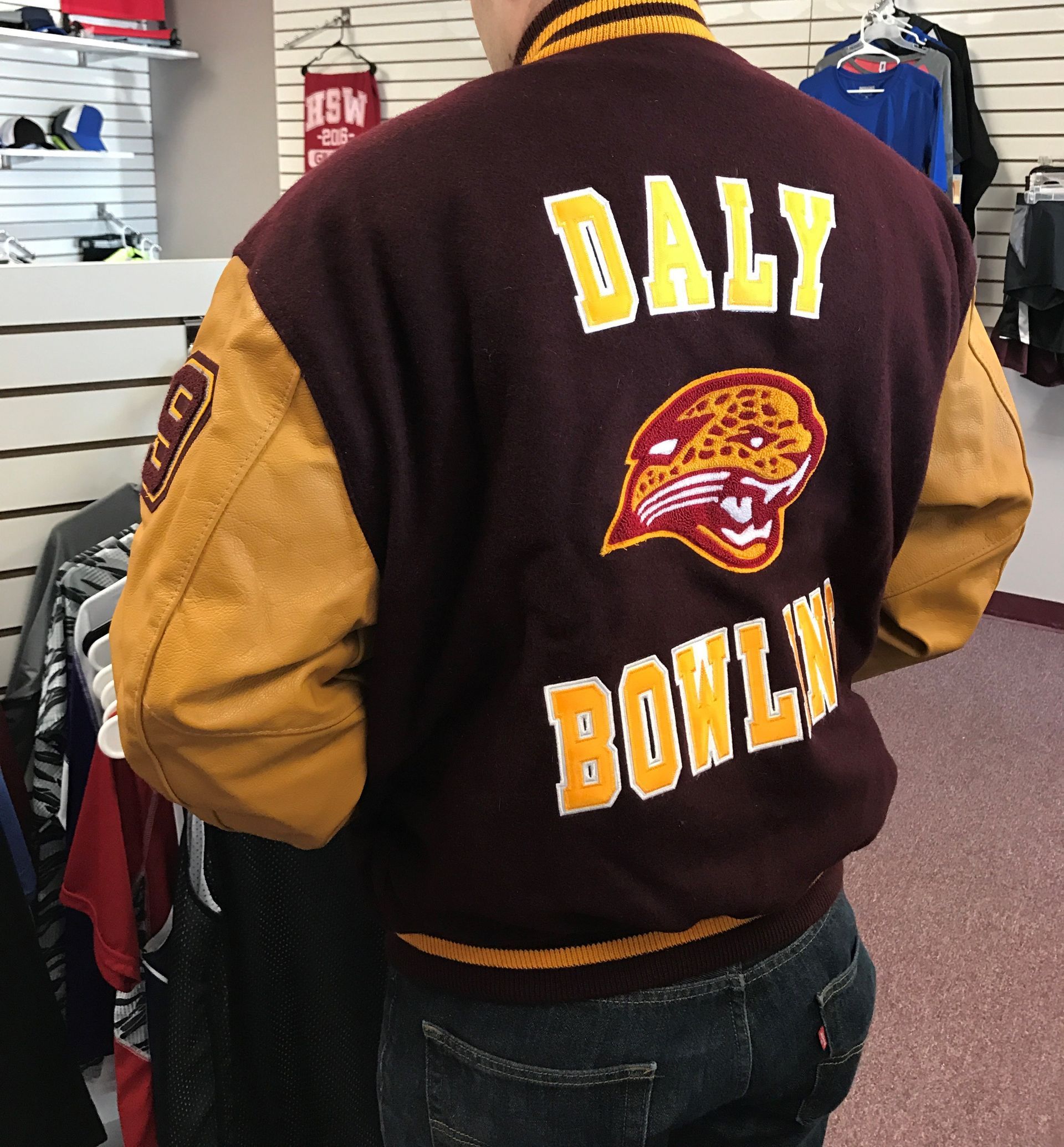 A person wearing a maroon and yellow jacket that says daly bowling