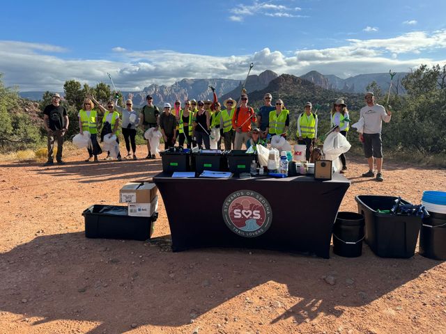 A group of people are standing around a table with mountains in the background.