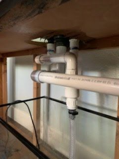 PVC plumbing system under a structure, with pipes and connectors in white and gray.
