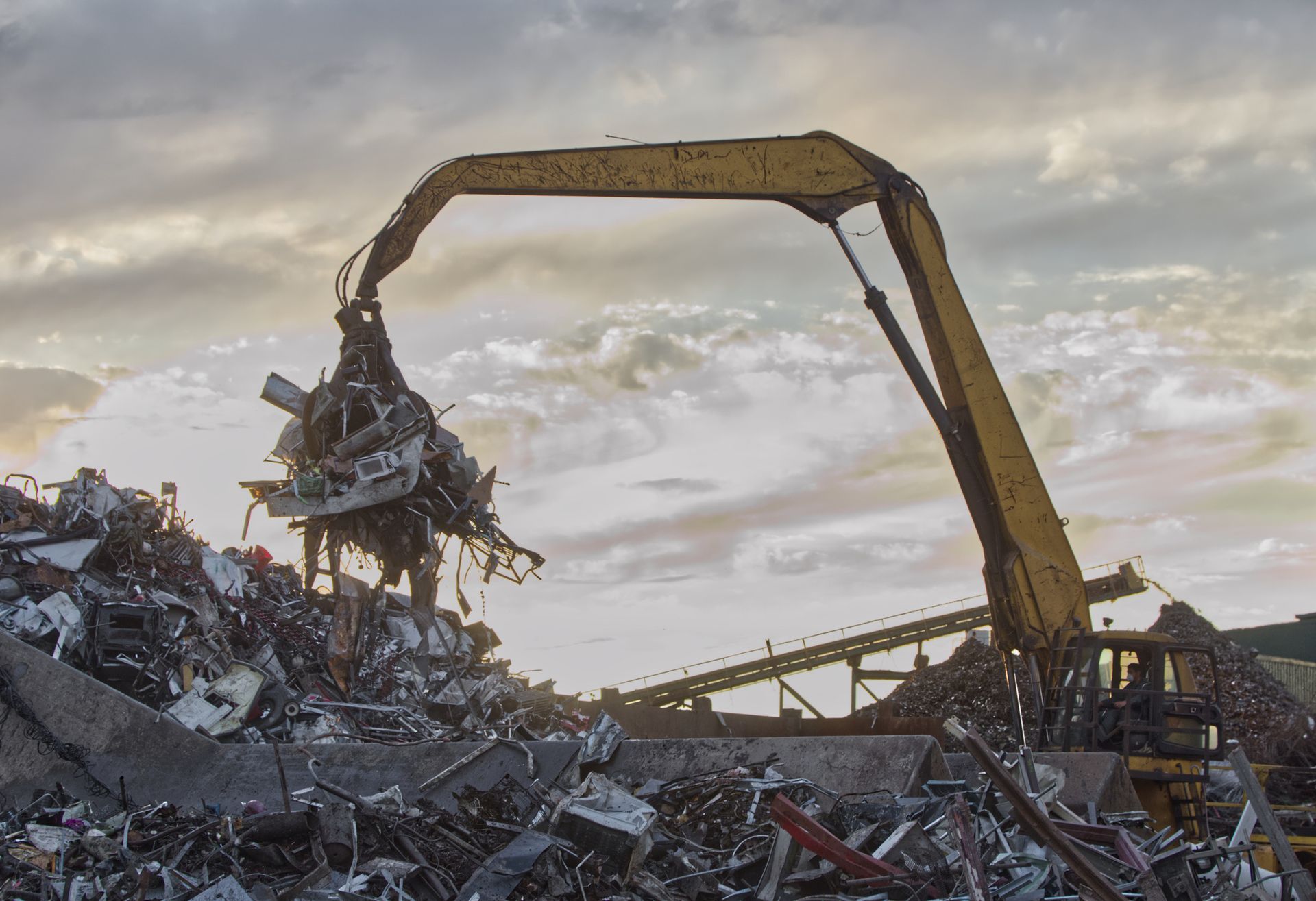 A hydraulic grabber lifts a heap of rusty metal during scrap metal recycling at an industrial yard.