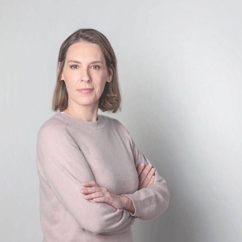 Eine Frau in einem rosa Pullover steht mit verschränkten Armen da.