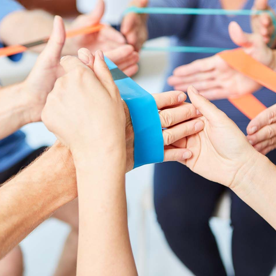 Hände von Menschen, die bunte Widerstandsbänder halten, möglicherweise für Therapie oder Training.