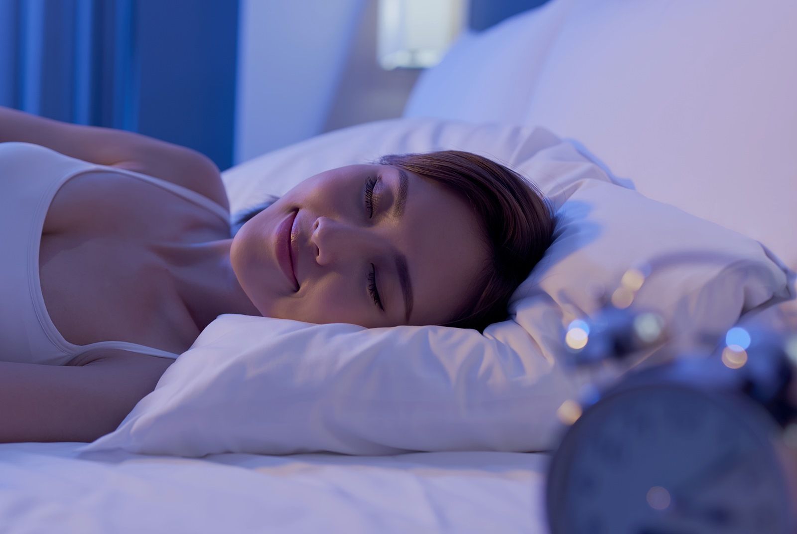 一個女人睡在鬧鐘旁的床上。