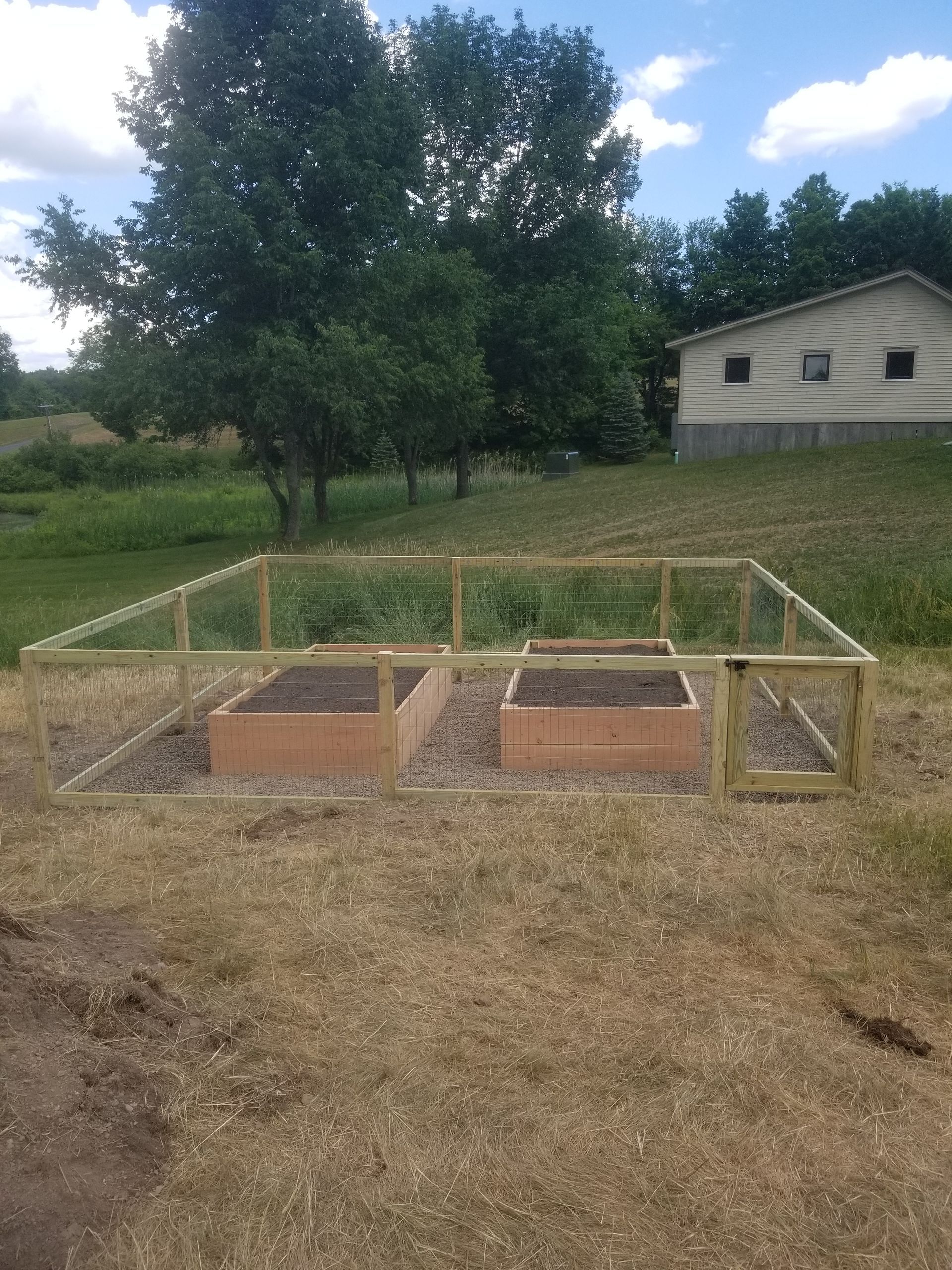 A wooden fence surrounds a garden with a house in the background