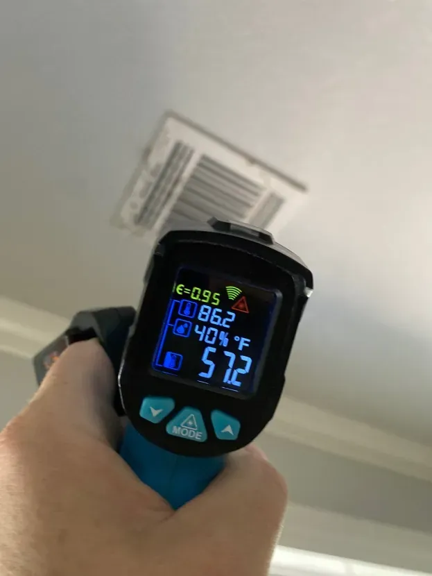 A person is holding a thermometer in front of a ceiling vent.