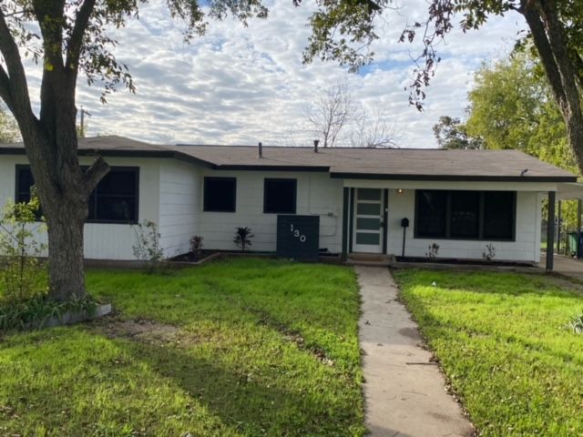 A white house with a brown roof and a tree in front of it.