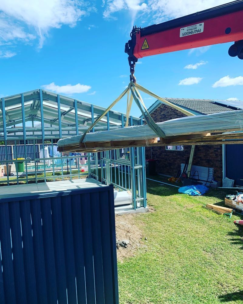 A Red Crane Lifts Wooden Planks Over a Steel-Framed Structure — Express Timber Solutions In Long Jetty, NSW