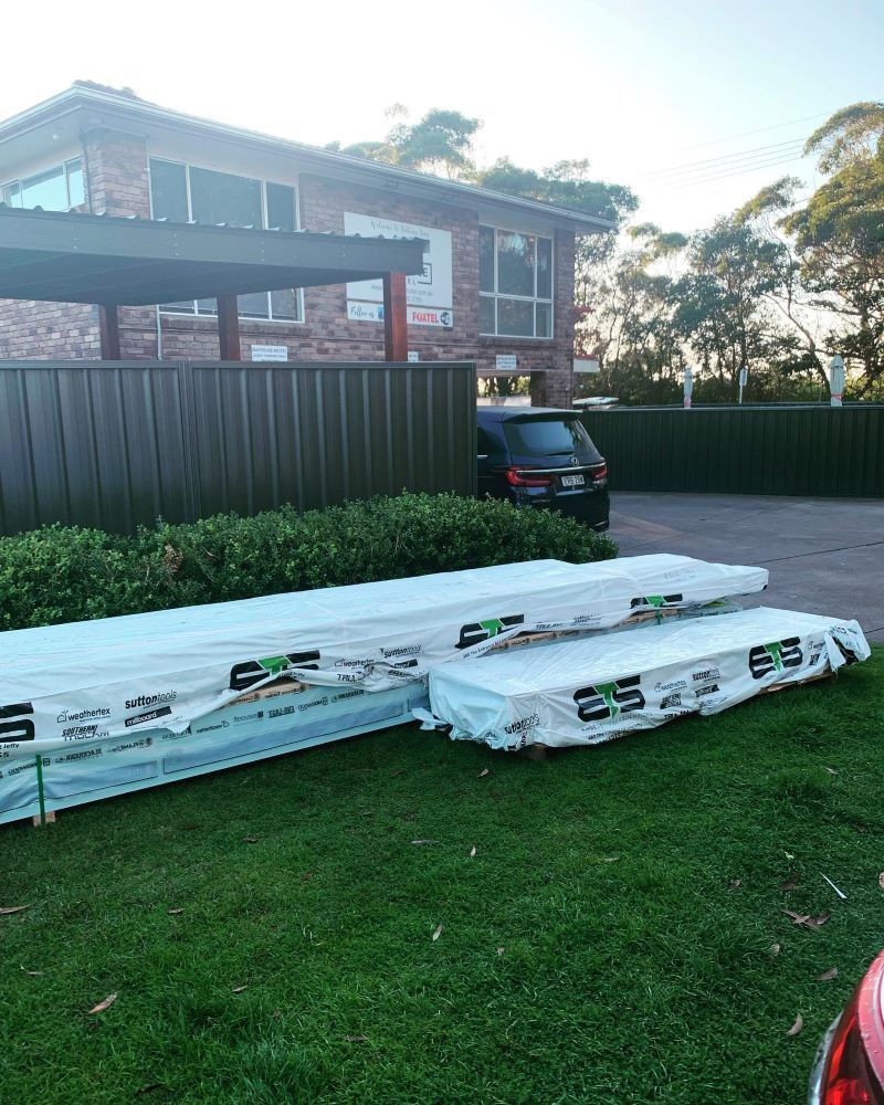 Two Stacks of Wrapped Lumber on A Grassy Lawn in Front of A Brick House — Express Timber Solutions In Long Jetty, NSW