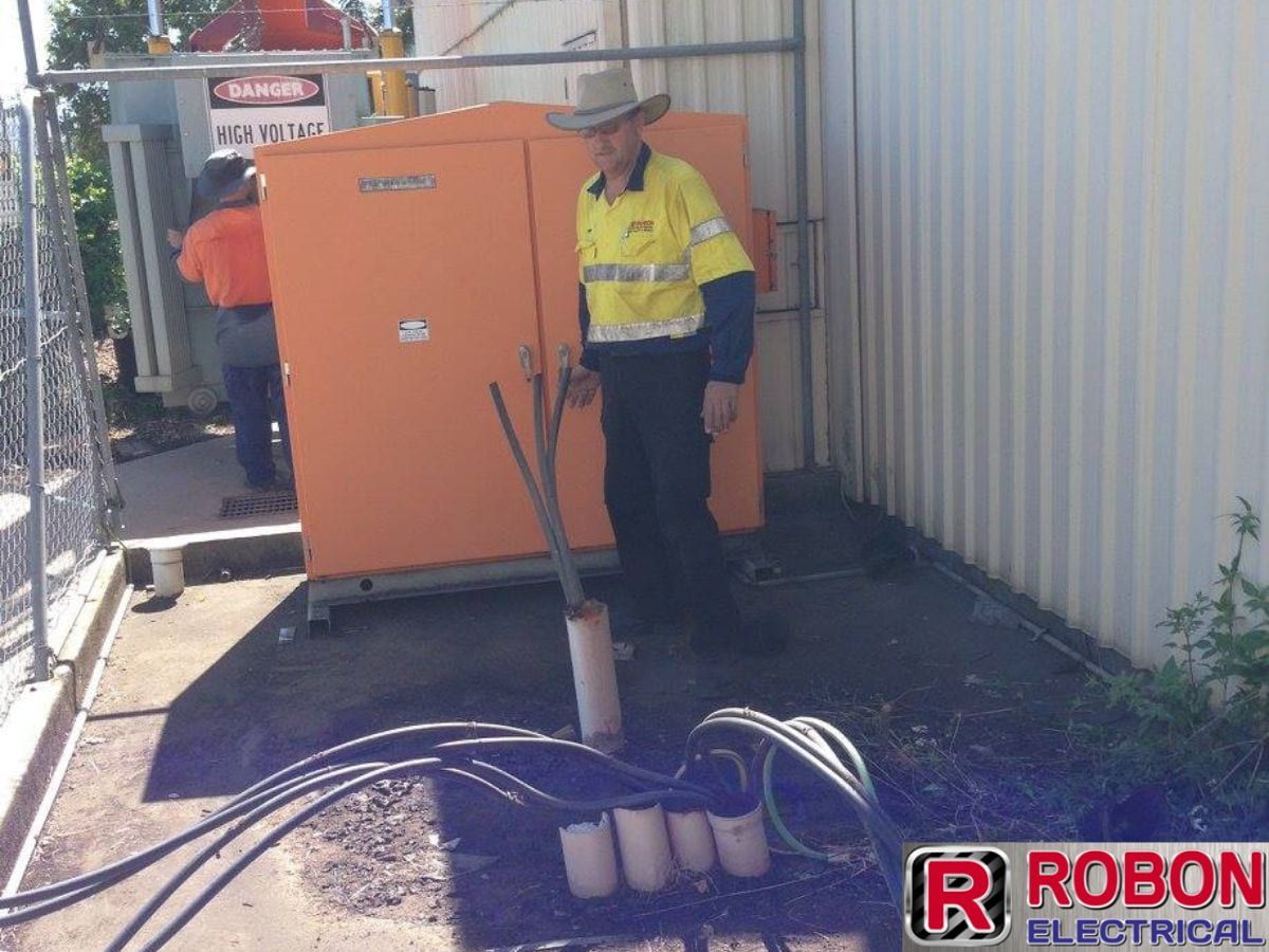 A Man Standing In Front Of An Orange Box That Says Robon Electrical — Robon Electrical In Holloways Beach, QLD