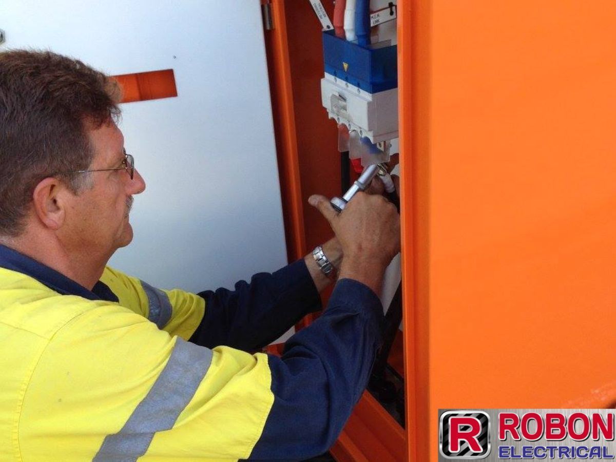 A Man Working On An Orange Box With Robon Electrical Written On It — Robon Electrical In Holloways Beach, QLD