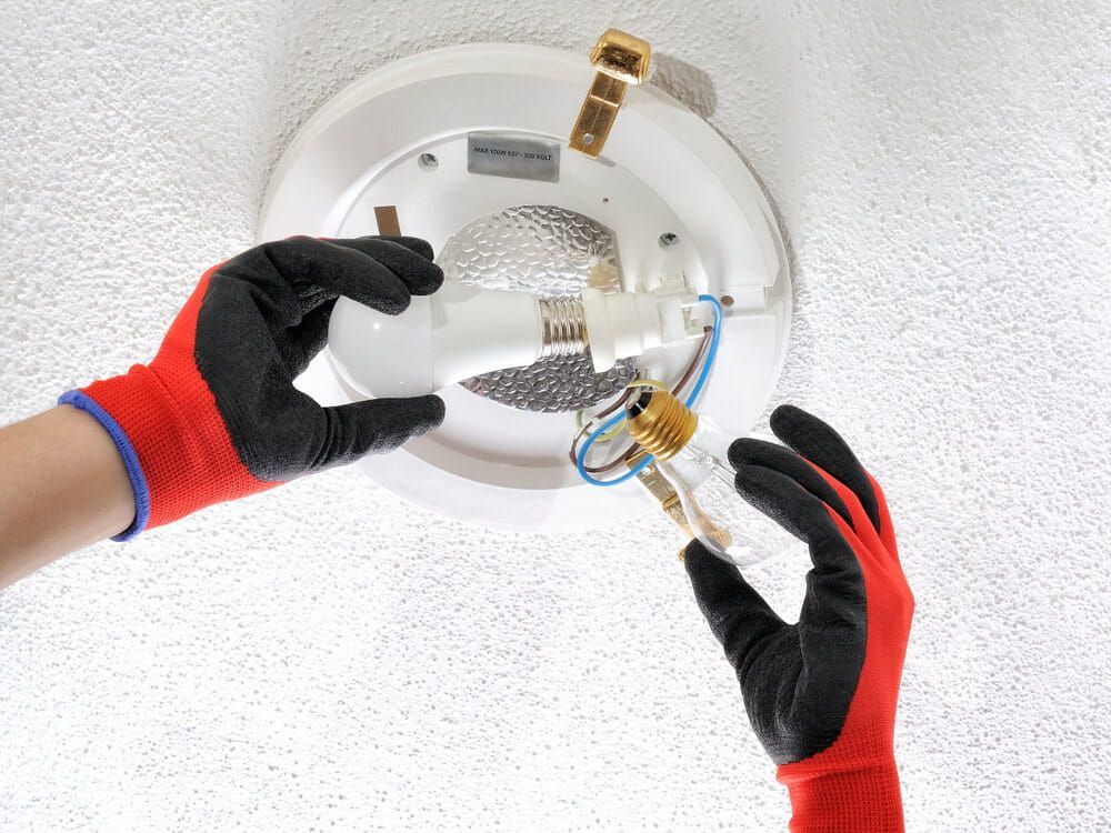A Person Wearing Red Gloves Is Changing A Light Bulb On A Ceiling — Robon Electrical In Holloways Beach, QLD