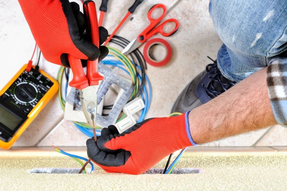 A Man Wearing Red Gloves Is Working On Electrical Wires — Robon Electrical In Holloways Beach, QLD