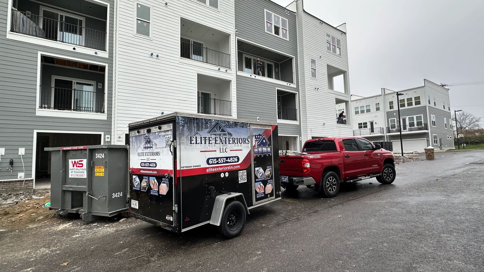 Red truck towing a black trailer with logo, parked near a partially built apartment building.