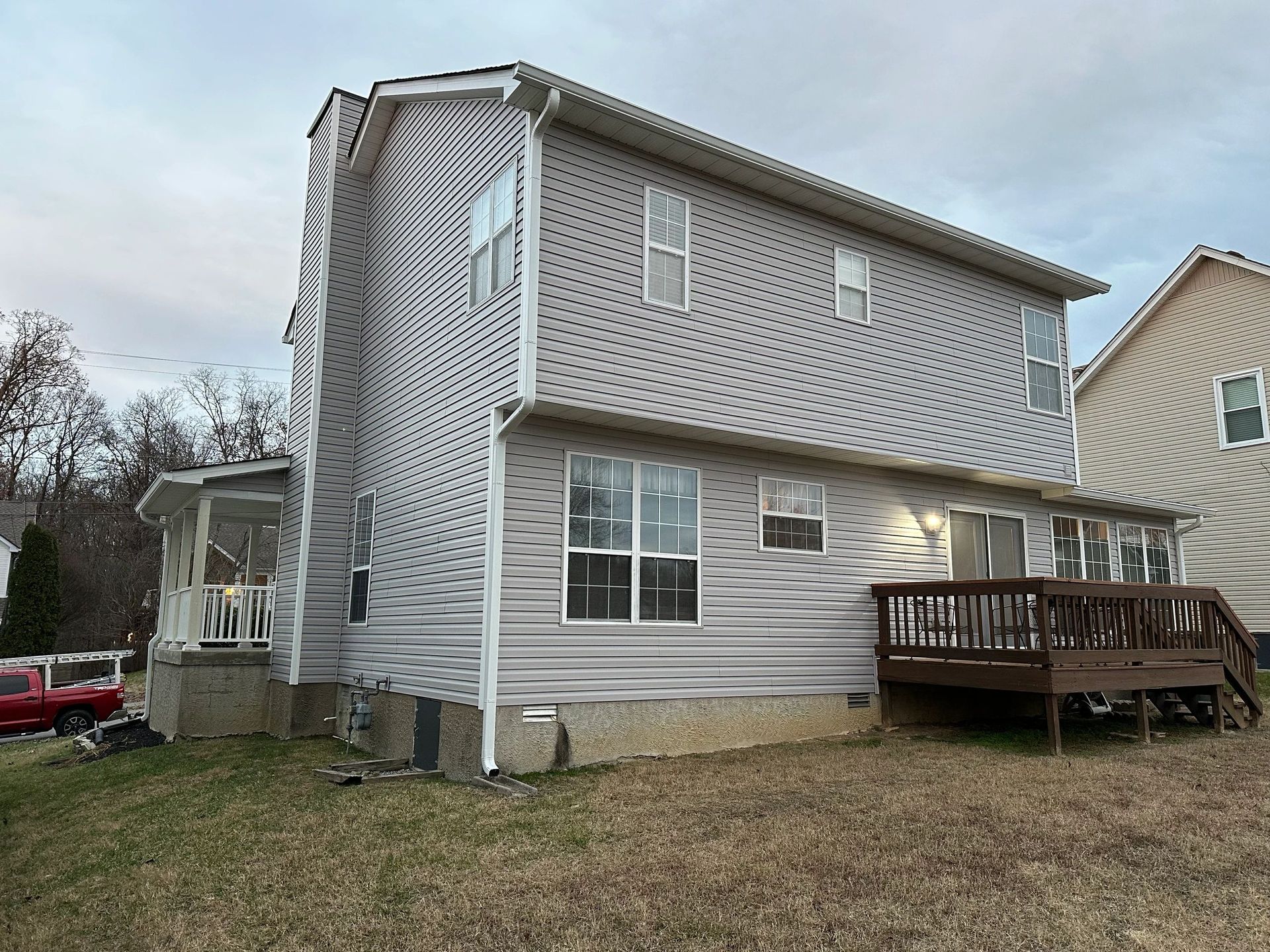 Back view of a two-story house with gray siding, a deck, and a screened-in porch on a cloudy day.