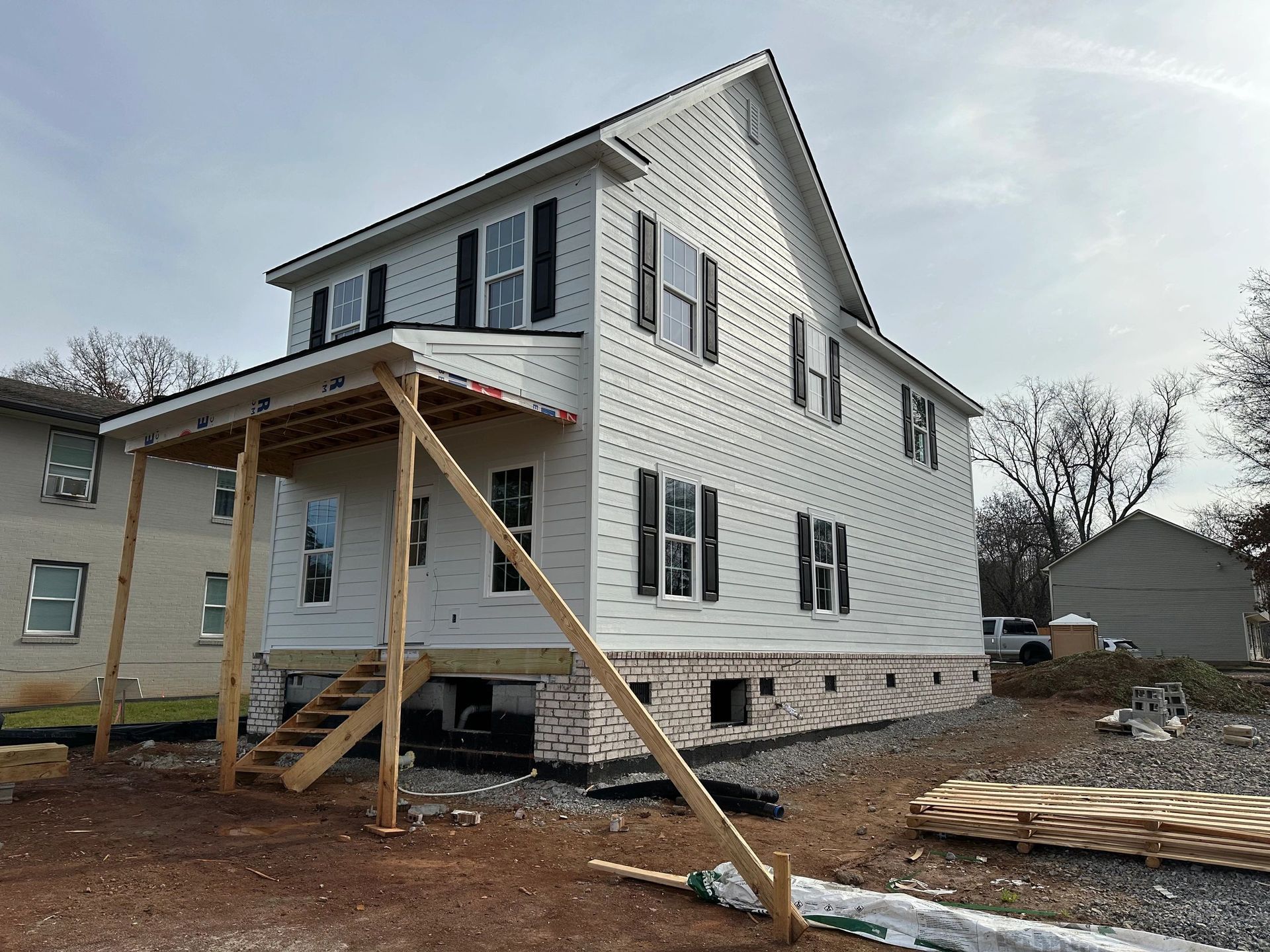 New two-story house under construction with white siding, black shutters, and a porch supported by wooden beams.