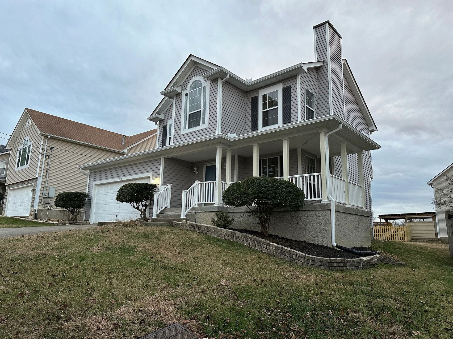 Two-story house with gray siding, porch, and chimney on a cloudy day.