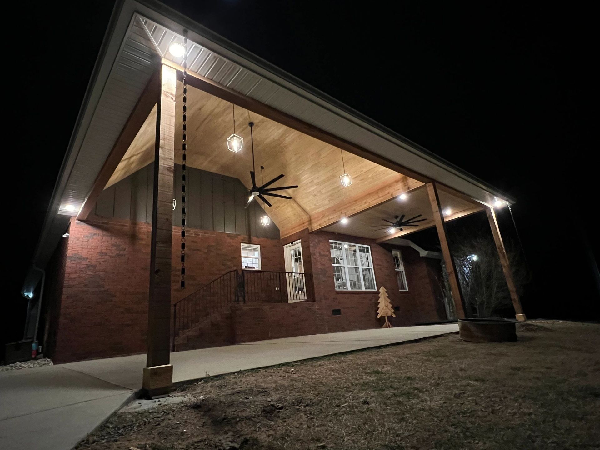 Brick house with a covered porch at night, lit by overhead lights and a fan.