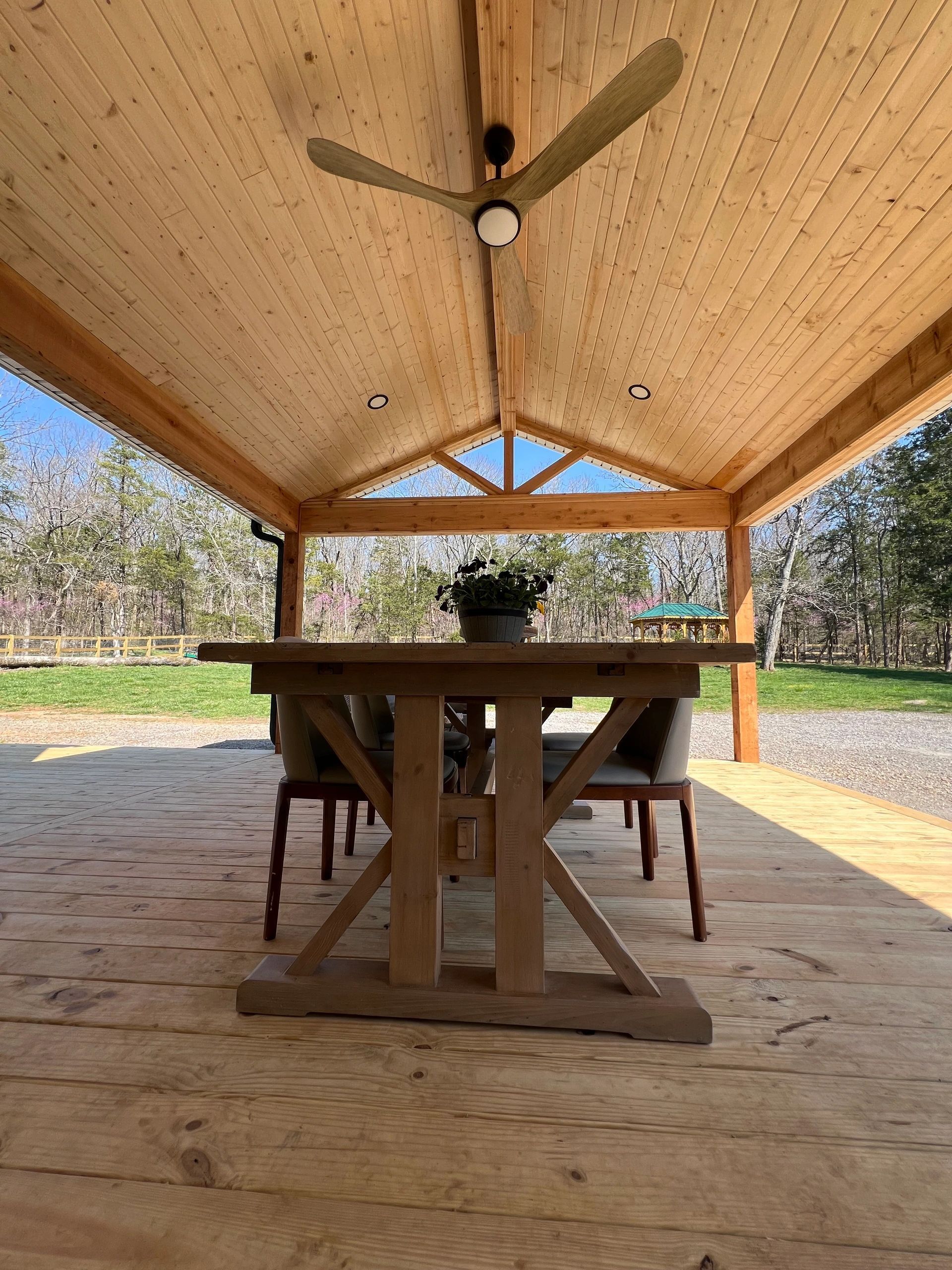 Wooden outdoor dining area with table, chairs, and ceiling fan.