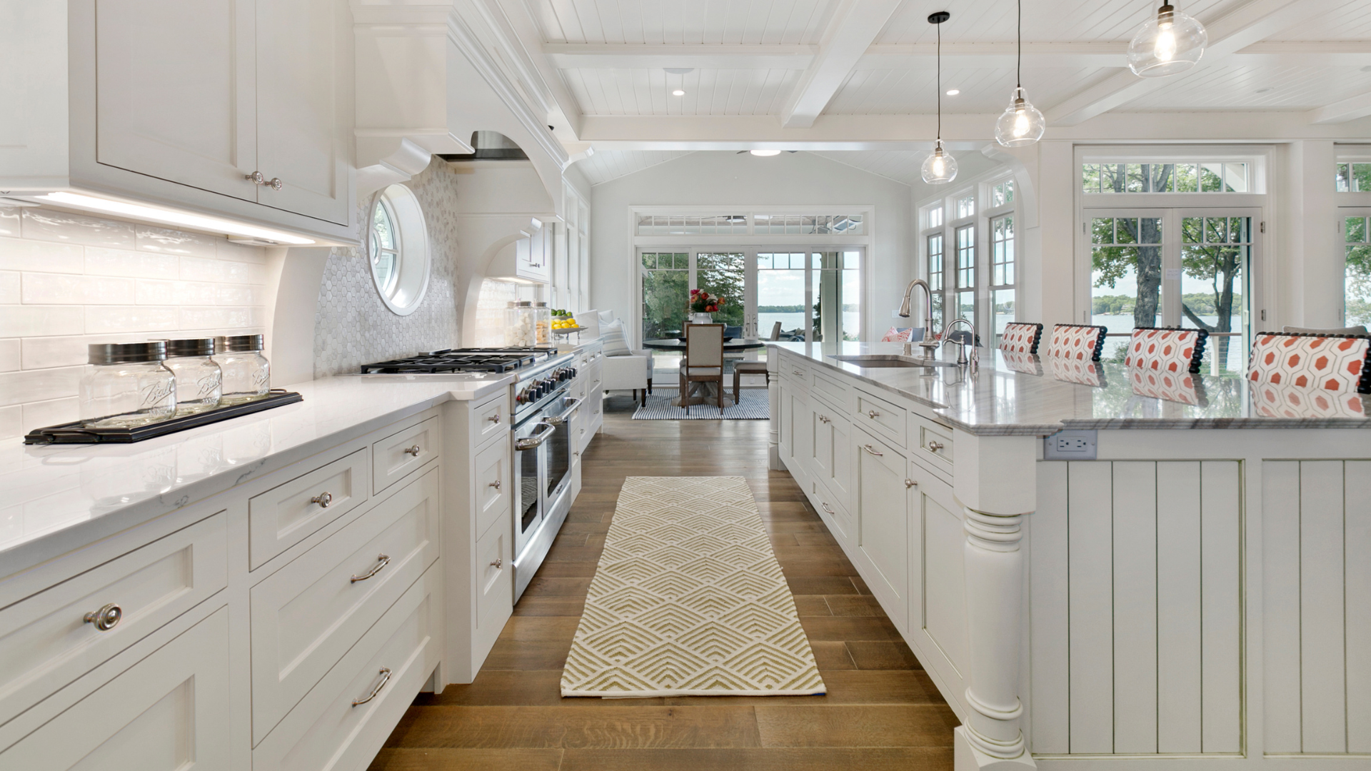 Bright, white kitchen with long island, wooden floors, and view of outdoor dining area.