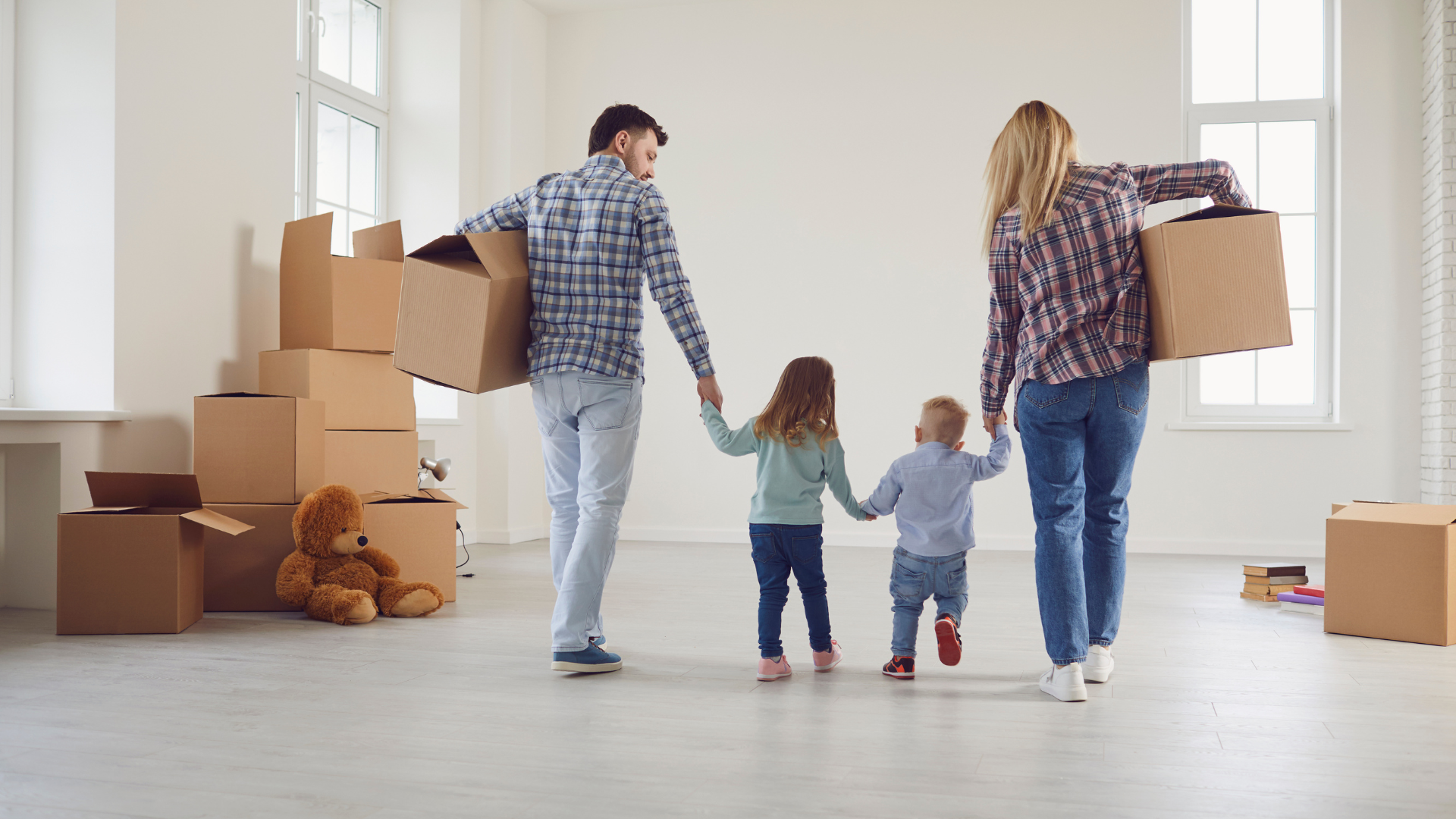 Family holding hands, carrying boxes into an empty house, excited about moving.