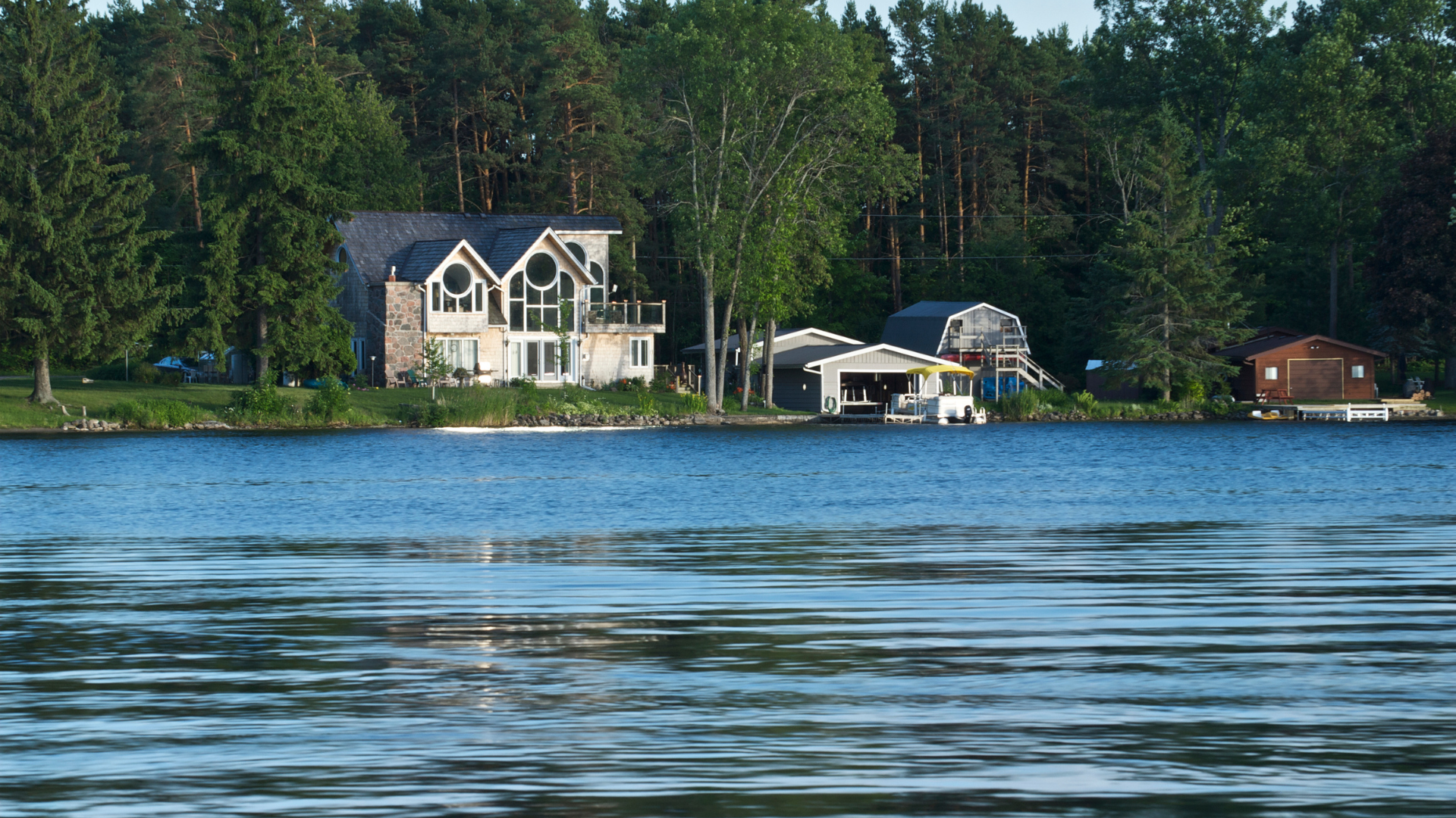 Lakeside house with multiple stories, a boat house, and trees reflected in the water.