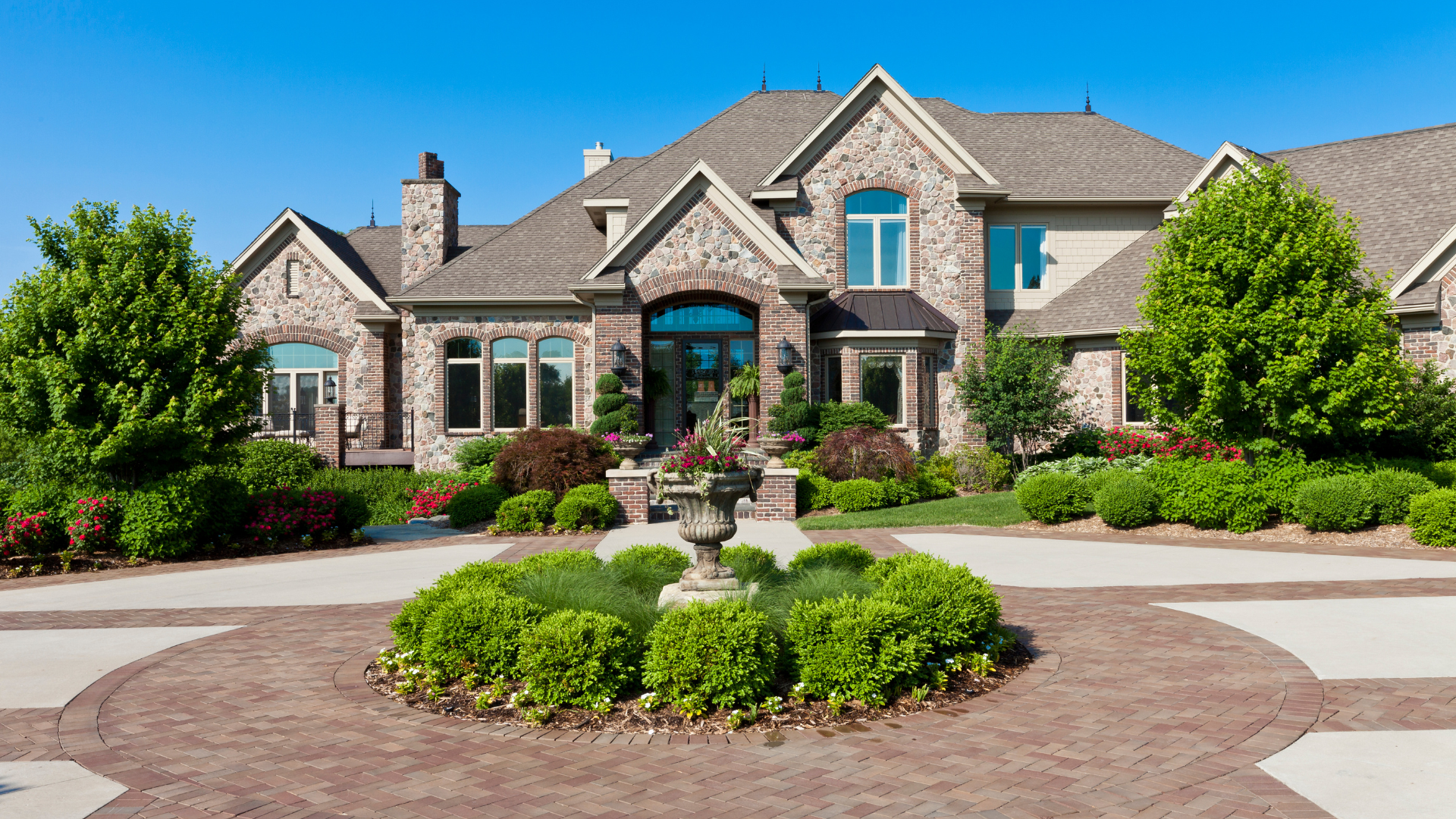 Large stone house with circular driveway, fountain, and lush landscaping.