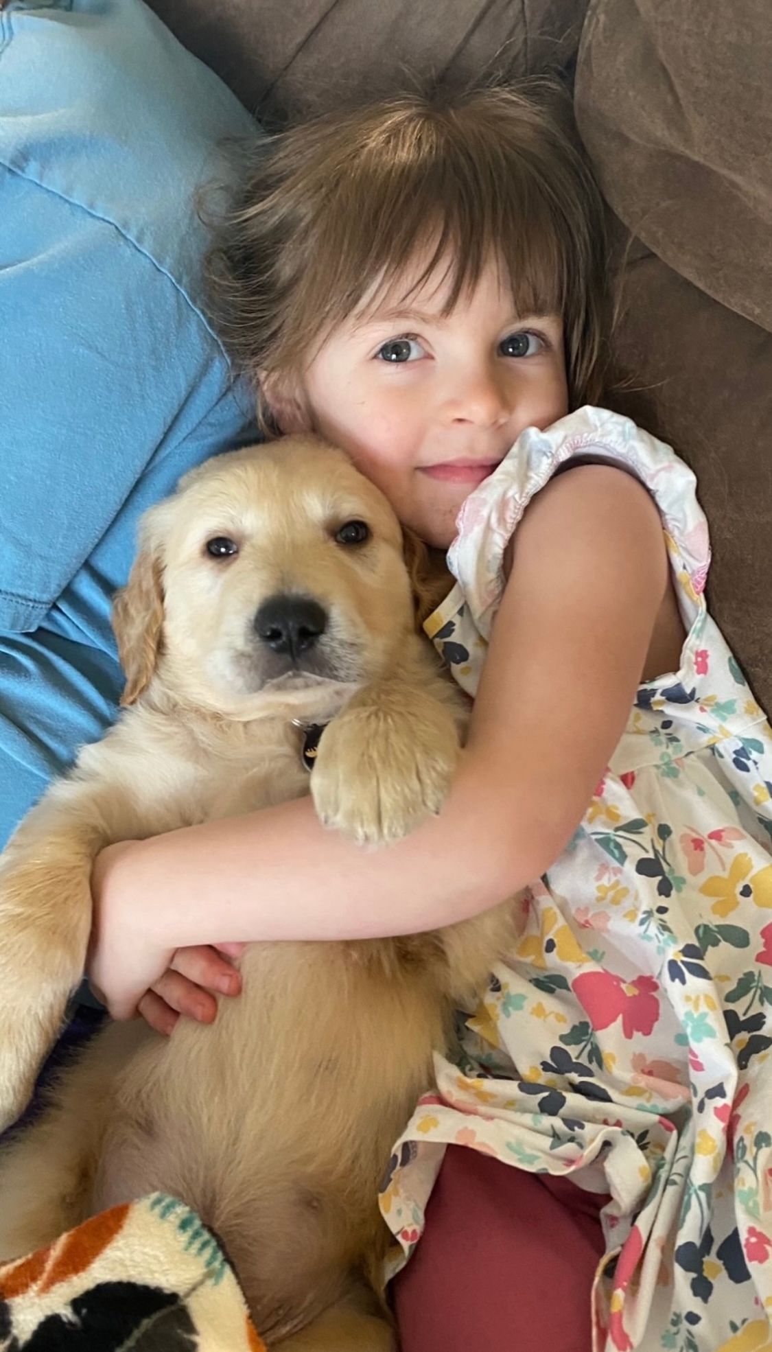 A little girl is holding a puppy on a couch.