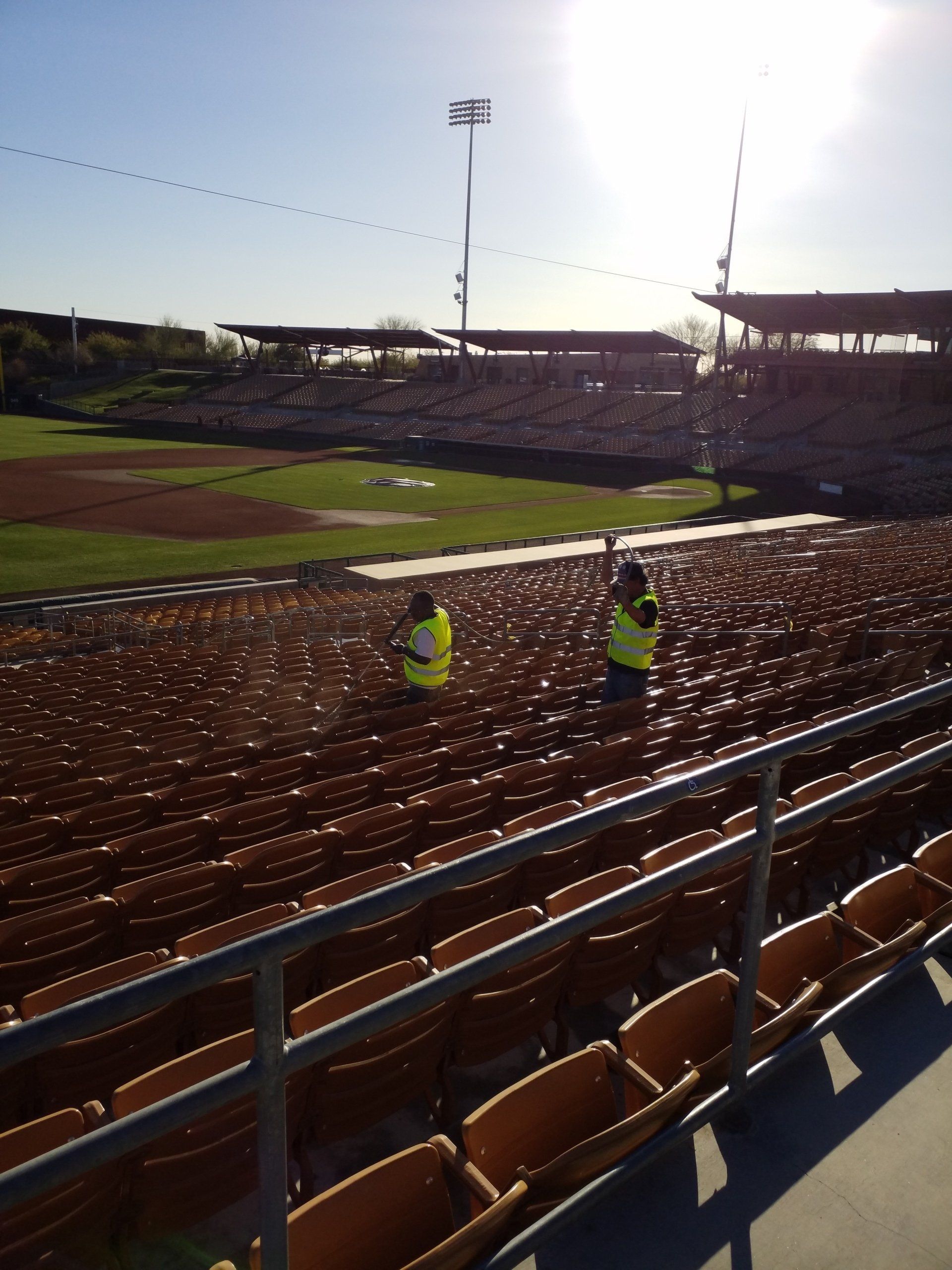 Two men in yellow vests are standing in the stands of a baseball stadium