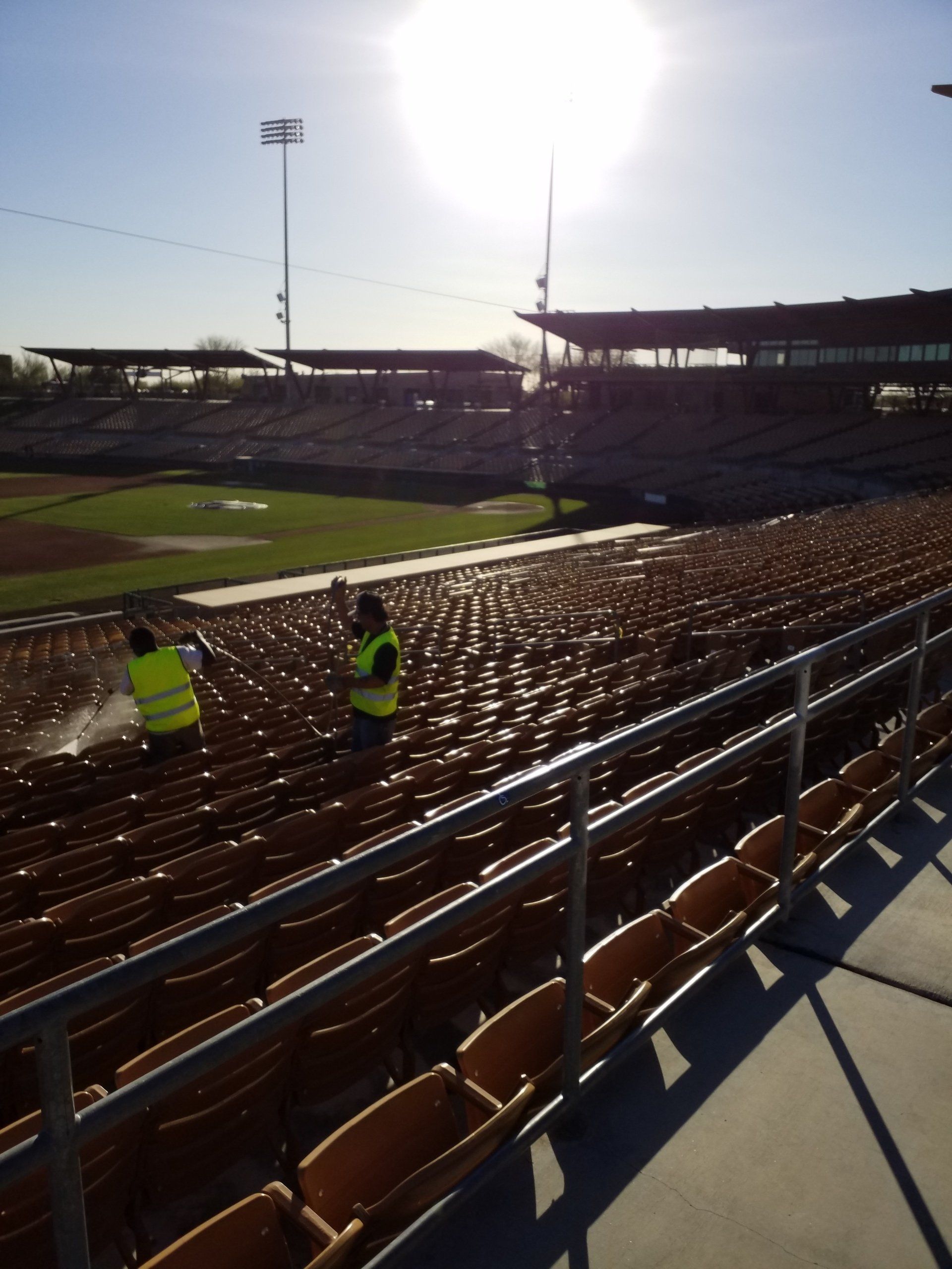 Two men in yellow vests are cleaning the seats of a baseball stadium