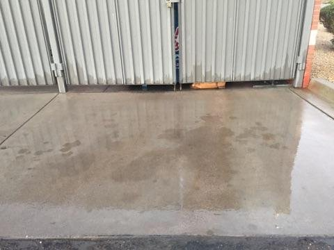 A concrete driveway with a fence in the background and a puddle of water on the ground.