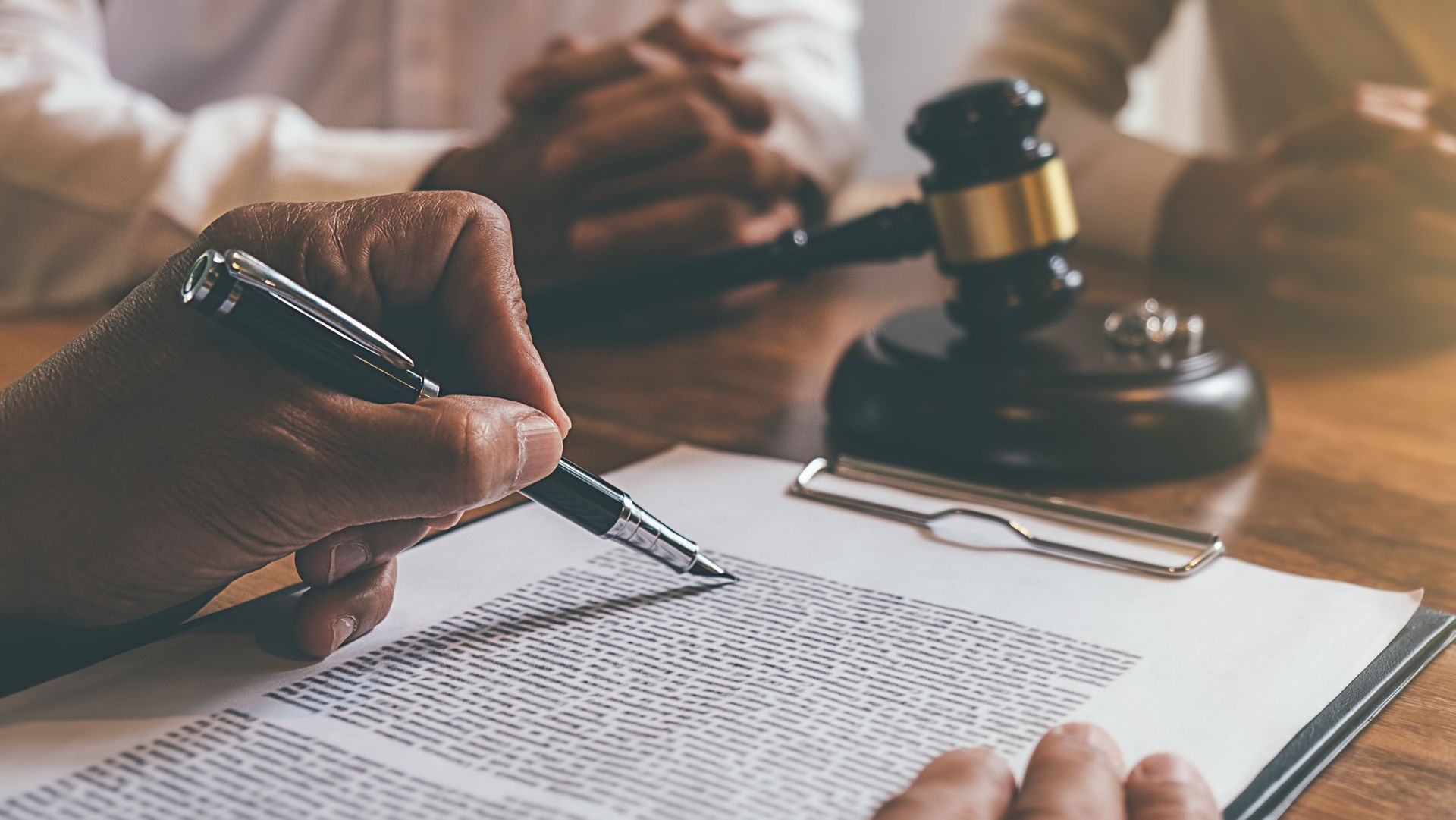 Person signing document, gavel and people at a wooden table.