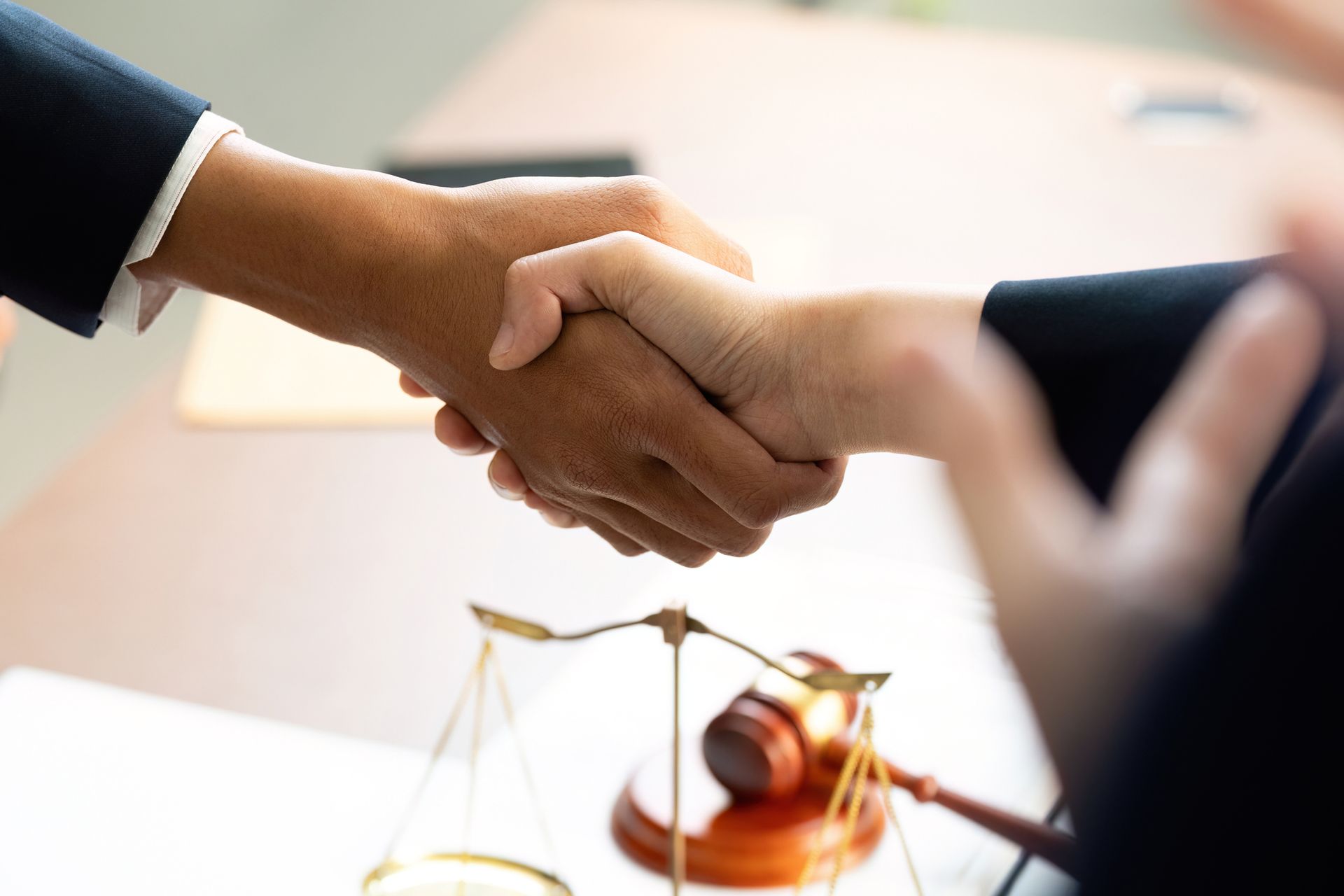 Two people shaking hands over a desk with a gavel and scales of justice.