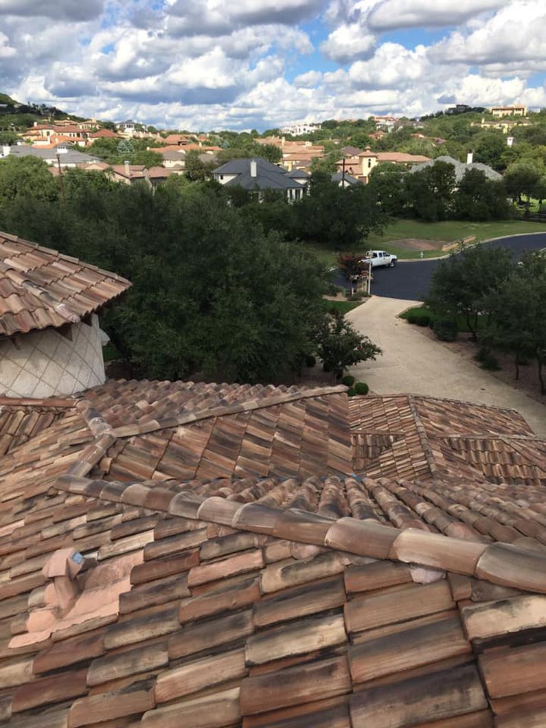 View from a clay tile roof over a residential area with trees and a cloudy sky.