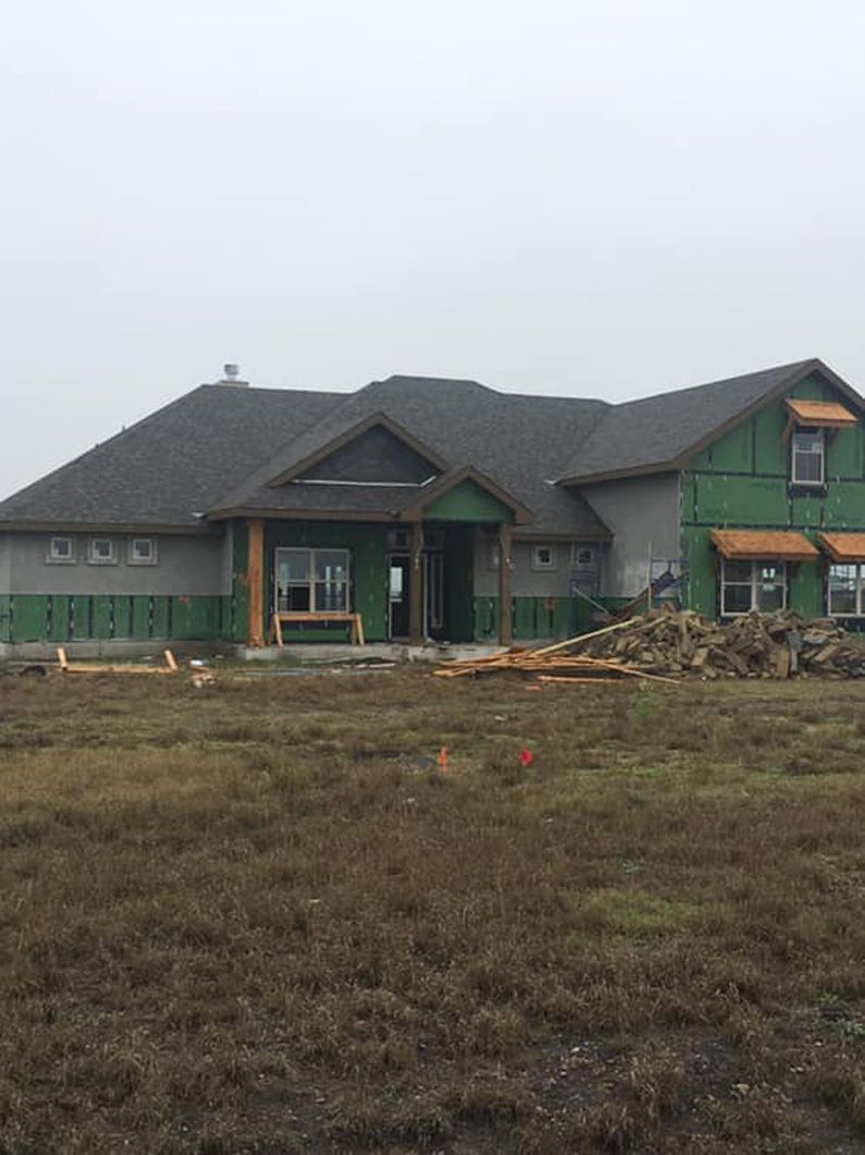 New house under construction, gray siding, green sheathing, wood framing, overcast day, grassy lot.
