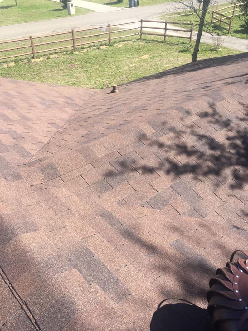 Brown shingled roof with shadows, overlooking a grassy area with a fence and path.