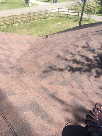 Brown shingle roof with shadows. View of a park with a fence and path in the background.