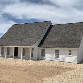 White house under construction with dark gray roof, light-colored siding, and a gravel yard.