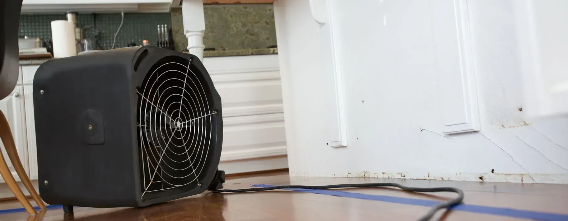 A black fan is sitting on a wooden floor in a room.