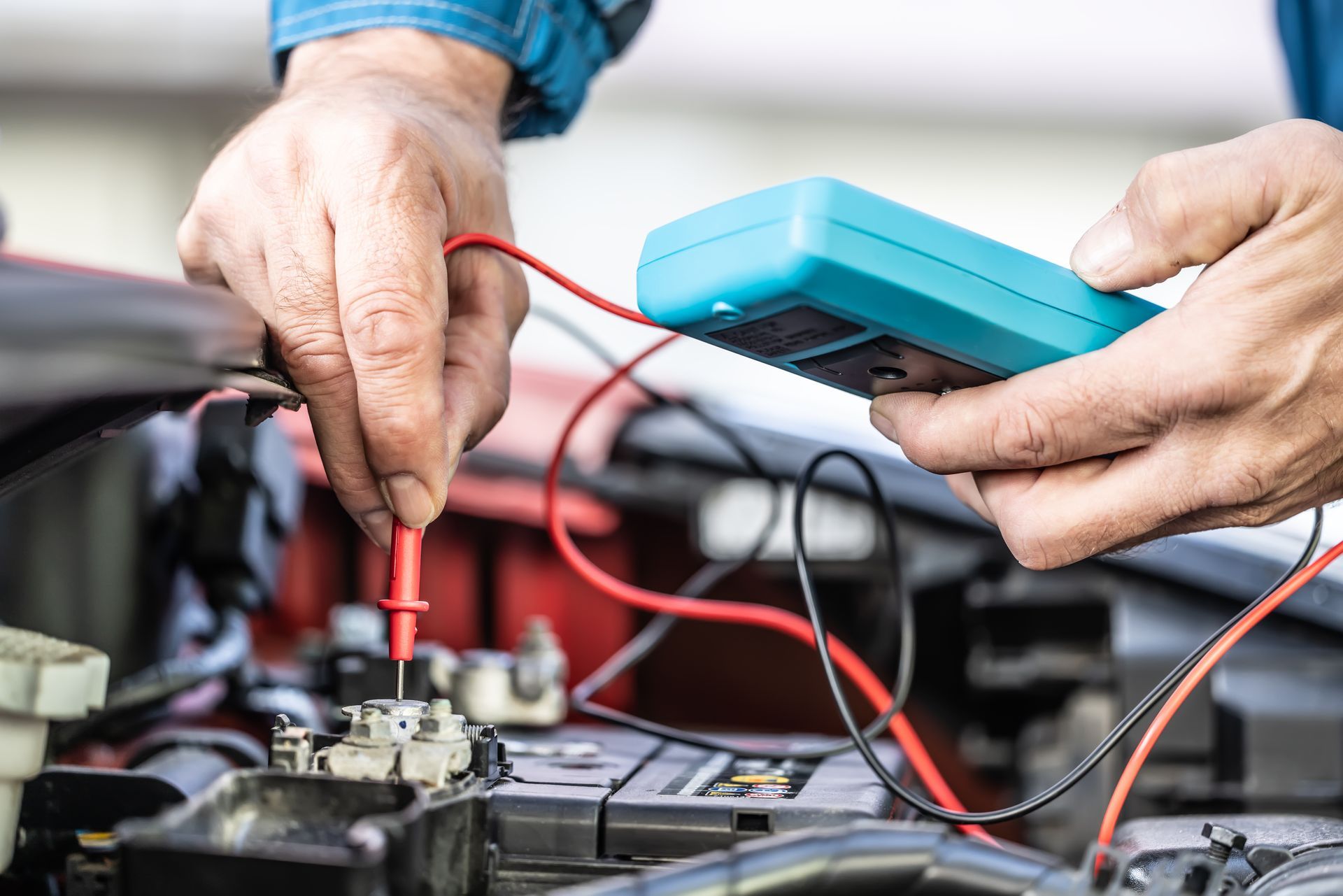Hands using a multimeter to check voltage on a car battery.