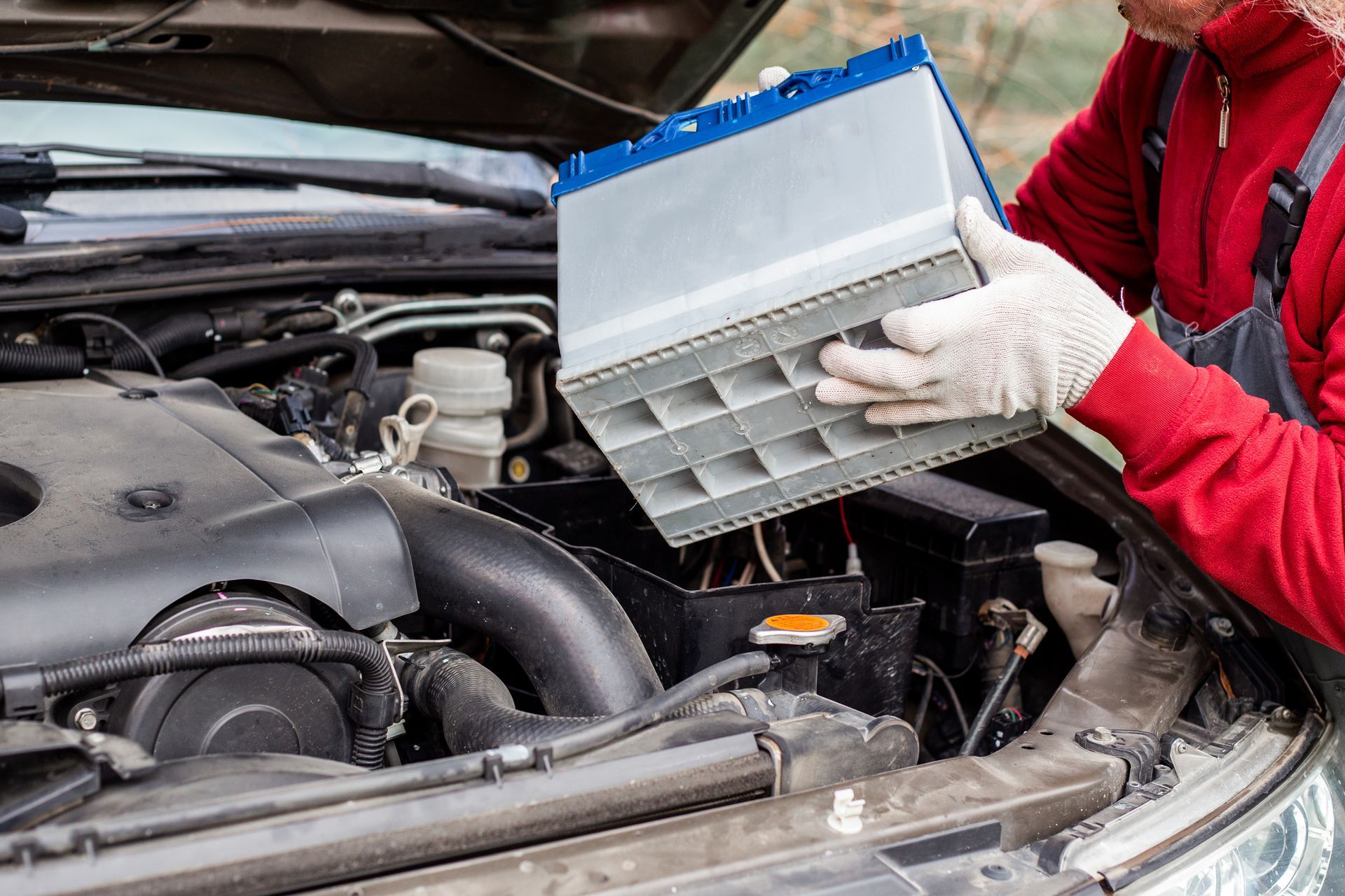 Car mechanic replacing a Gray auto battery of a car with gloves on Car mechanic replacing a Gray auto battery of a car with gloves on
