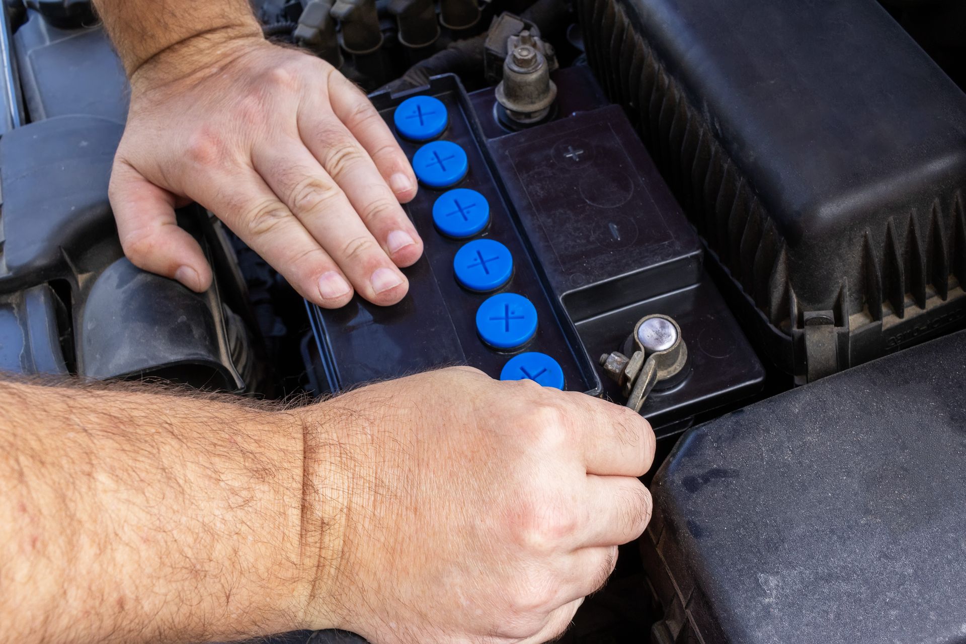 Hands connecting terminals of new Odyssey Battery in car for secure and reliable power.