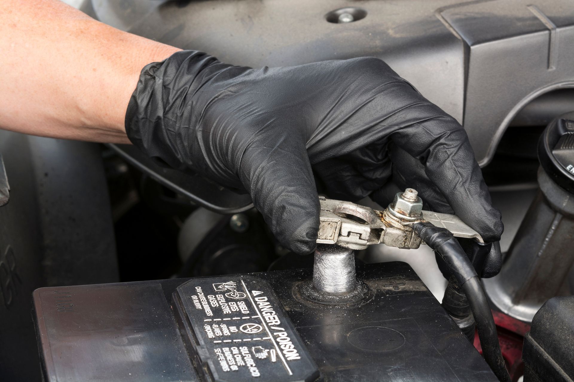 Close-up of a gloved hand as it installs a battery terminal, using a wrench, to a car battery.