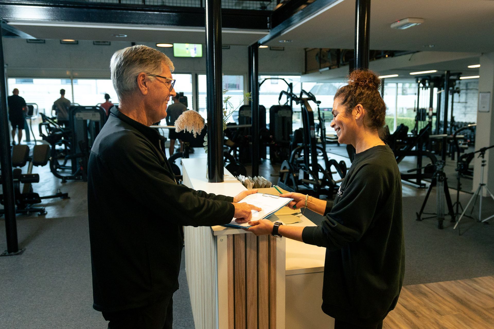 een man hurkt om een halter op te tillen in een sportschool.