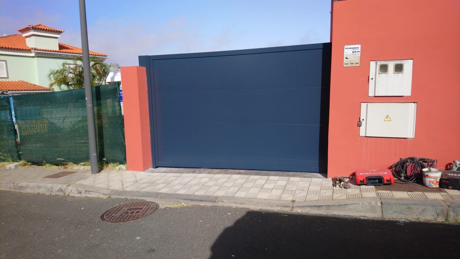 Puerta azul oscuro, paredes rojas y acera gris; fachada de edificio con cajas eléctricas.