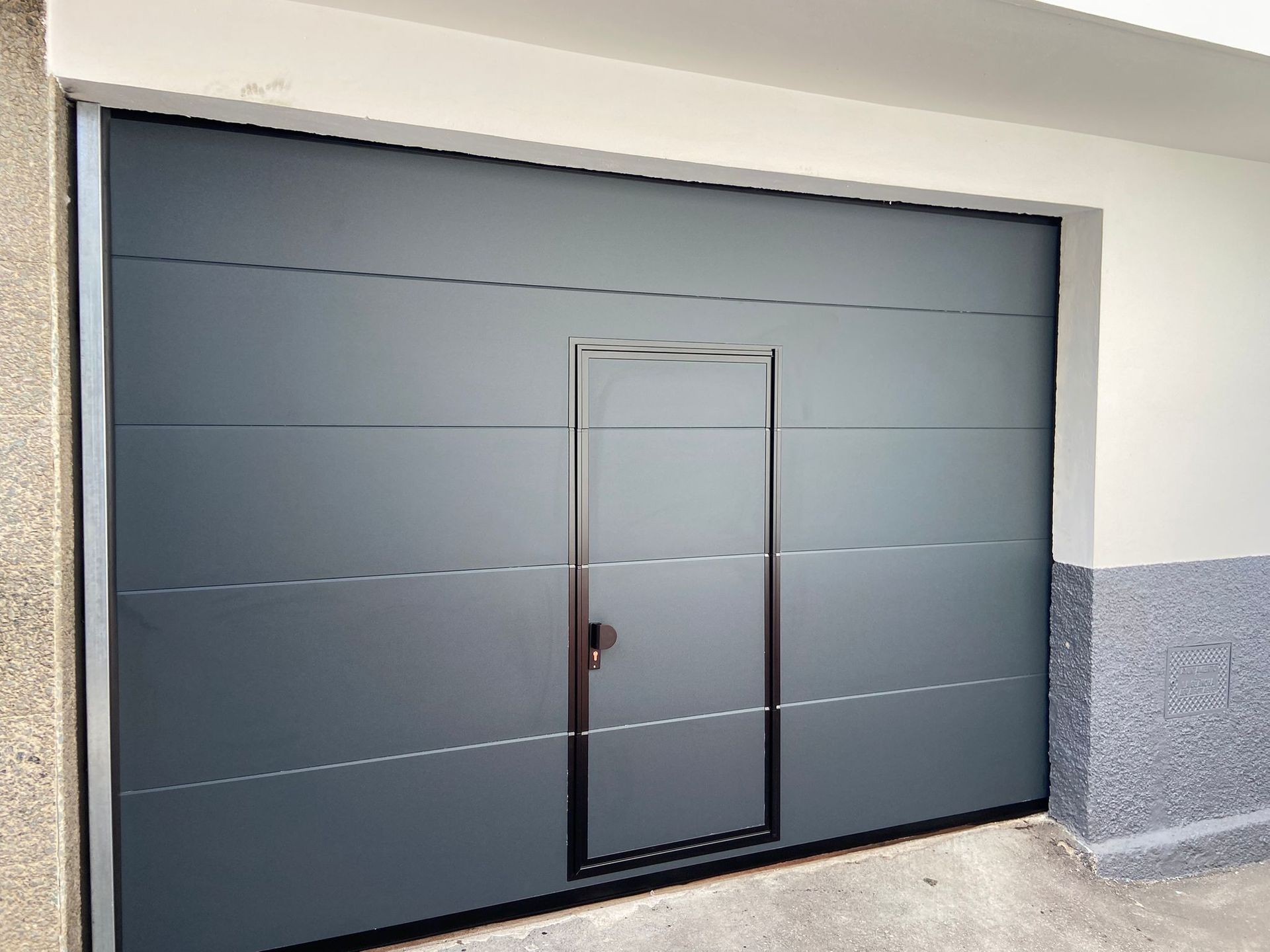 Puerta de garaje gris con una puerta más pequeña insertada.