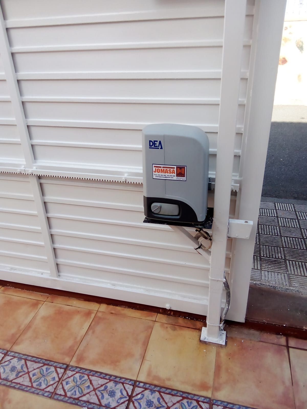 Una puerta blanca con apertura automática; suelo de baldosas marrones.