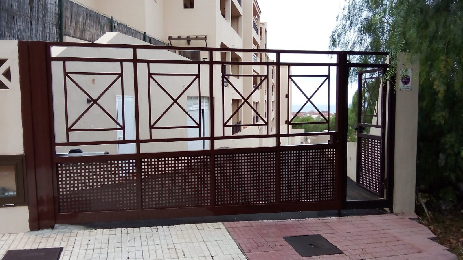 Puerta corrediza de metal marrón frente a un edificio con elementos de diseño geométrico.