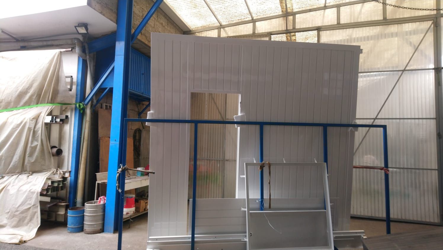 Estructura metálica blanca con marco de puerta y soportes azules, en el interior de un taller.